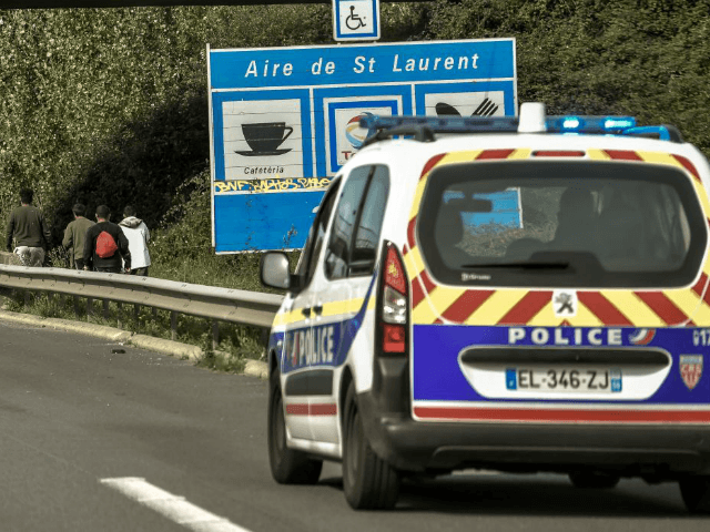 Police ride a car as they watch migrants walking along the A25 motorway in the direction o