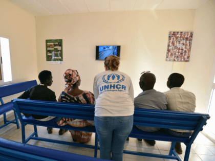 A UNHCR representative (C) speaks with refugees as they watch television in a UNHCR buildi
