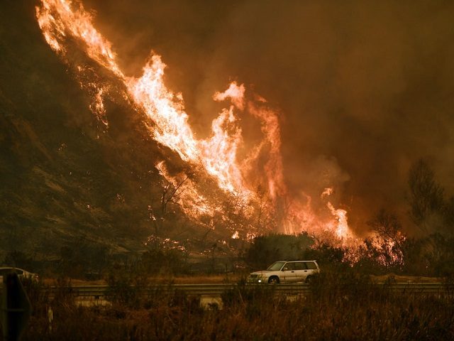 TOPSHOT - Vehicles pass beside a wall of flames on the 101 highway as it reaches the coast during the Thomas wildfire near Ventura, California on December 6, 2017. California motorists commuted past a blazing inferno Wednesday as wind-whipped wildfires raged across the Los Angeles region, with flames triggering the …