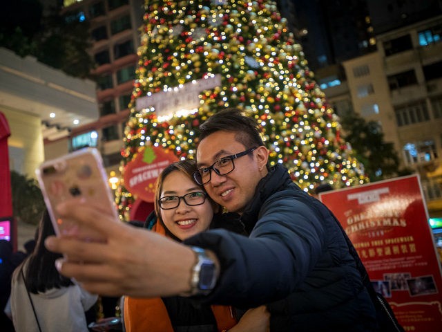 People take a selfie photograph with an Apple Inc. iPhone in front of an illuminated Christmas tree in Hong Kong, China, on Saturday, Dec. 9, 2017. With more Chinese tourists likely to travel to Hong Kong next year as the yuan strengthens against the Hong Kong dollar, retailers are poised to …