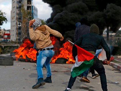 Palestinian demonstrators holding a national flag throw stones towards Israeli troops during clashes that followed protests against a decision by US President Donald Trump to recognise Jerusalem as the capital of Israel, in the West Bank city of Ramallah on December 7, 2017. / AFP PHOTO / ABBAS MOMANI (Photo …