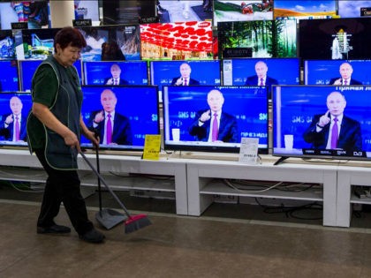 A cleaner walks past TV sets showing Russian President Vladimir Putin during his annual li