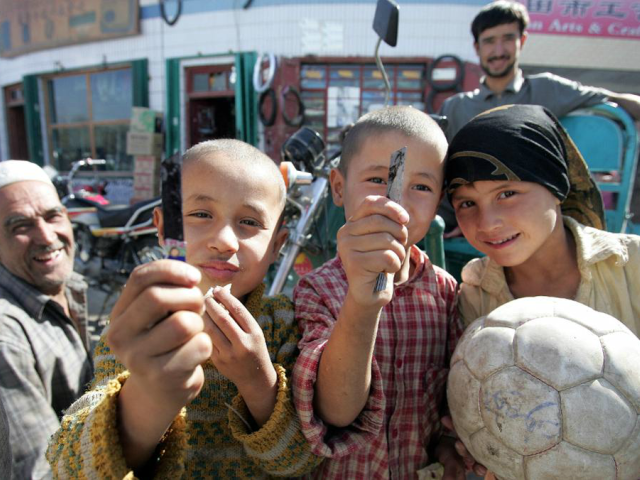 Young Uighur boys display their switch-blades while posing with a girl holding a soccer ba