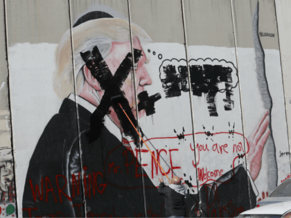 A Palestinian paints over a poster of the U.S. President Donald Trump during a protest in