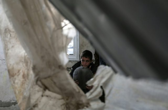 A Palestinian child rescues belongings from his home which was damaged in an Israeli air s