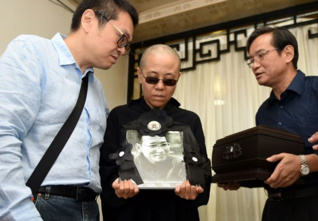 Liu Xia (C) holds a portrait of her late husband, Nobel laureate Liu Xiaobo, after his de