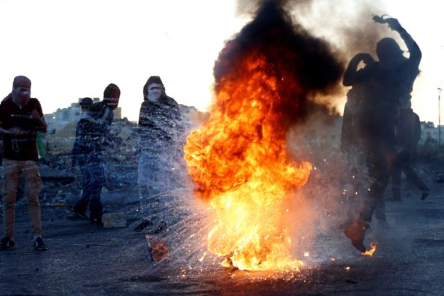 A Palestinian protester kicks a burning tyre during clashes with Israeli forces in the Wes