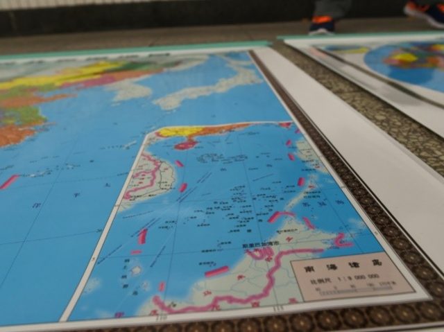In this photo taken on June 15, 2016 a vendor stands behind a map of China including an insert with red dotted lines showing China's claimed territory in the South China Sea