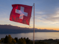 GettyImages-858570112 A Swiss flag is seen floating at sunset above Lake Geneva on October 5, 2017 from the Mont de Gourze in Riez, western Switzerland. / AFP PHOTO / Fabrice COFFRINI (Photo credit should read FABRICE COFFRINI/AFP/Getty Images)