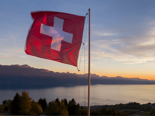 A Swiss flag is seen floating at sunset above Lake Geneva on October 5, 2017 from the Mont de Gourze in Riez, western Switzerland. / AFP PHOTO / Fabrice COFFRINI (Photo credit should read FABRICE COFFRINI/AFP/Getty Images)