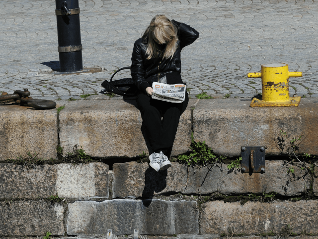 A girl reads a newspaper on a dock of Stockholm during sunny day in Stockholm on May 2, 20