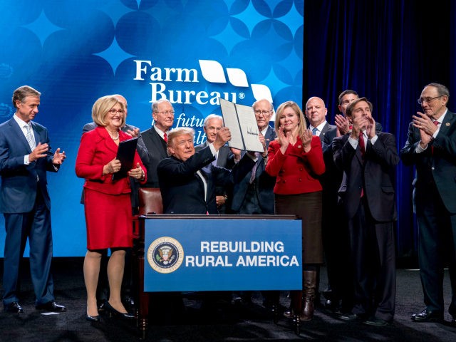 President Donald Trump holds up a signed executive order and a memorandum on rural broadba