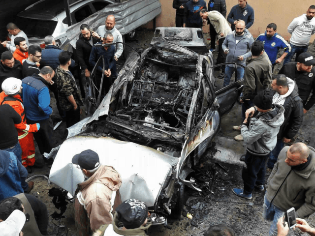 Residents look at a car that was destroyed in a bombing, in the southern port city of Sido