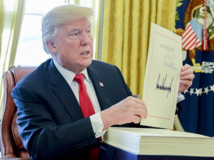 U.S. President Donald Trump holds up a tax-overhaul bill after singing it into law in the Oval Office of the White House in Washington, D.C., U.S., on Friday, Dec. 22, 2017. This week House Republicans passed the most extensive rewrite of the U.S. tax code in more than 30 years, …