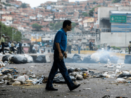 A man crosses a street blocked with garbage bags during a protest against Maduro in Caracas, on May 2, 2017. Armed "collectives" pressure low income urban dwellers from joining the protest movement, forcing them to share the view of the ruling Socialists United Party that the political opposition is orchestrating …