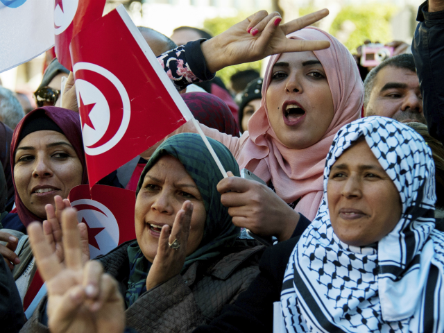 A Tunisian woman holds the national flag and make a sign during a rally to mark seven year