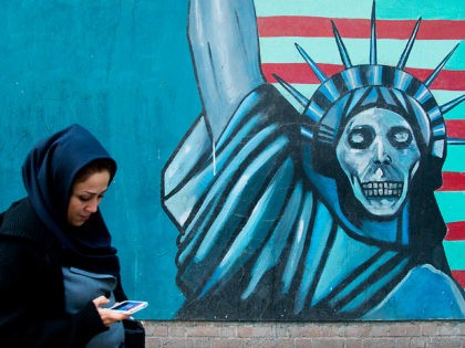 TEHRAN, IRAN - DECEMBER 20: Woman with phone passing in front of an anti-american propoganda slogan depicting statue liberty skeleton on the wall of the united states embassy, central district, tehran, Iran on December 20, 2015 in Tehran, Iran. (Photo by Eric Lafforgue/Art in All of Us/Corbis via Getty Images)