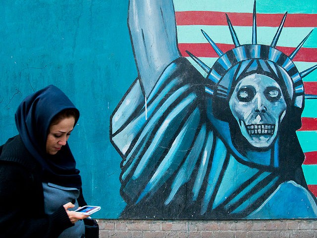 TEHRAN, IRAN - DECEMBER 20: Woman with phone passing in front of an anti-american propogan