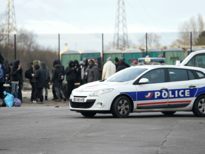 A police vehicle passes by people gathering in Calais, northern France, on February 2, 2018, a day after a large brawl between a hundred migrants resulted in several injuries. Four migrants were in critical condition after being shot and more than a dozen others were injured, some seriously, during clashes …