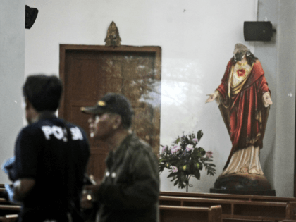 In this image shot through a glass window, police investigators examine the interior of St. Lidwina Church that was damaged following an attack in Sleman, Yogyakarta province, Indonesia, Sunday, Feb. 11, 2018. Police shot a sword-wielding man who attack the church during a mass, injuring a number of people including …