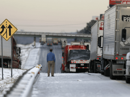 A man stands on the frozen roadway as he waits for traffic to clear along Interstate 75 Wednesday, Jan. 29, 2014, in Macon, Ga. A winter storm dumped snow and covered parts of the state with ice. Gov. Nathan Deal said early Wednesday that the National Guard was sending military …
