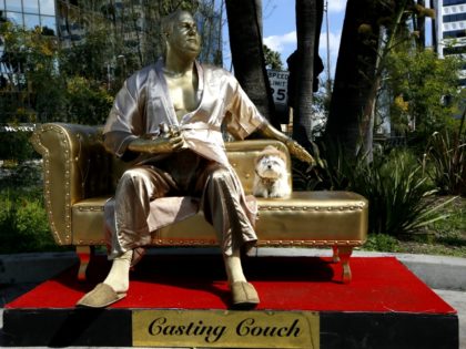 A dog named "Sassi" sits next to a golden statue of a bathrobe-clad Harvey Weinstein, seated atop a couch on the sidewalk along Hollywood Blvd., in Los Angeles Thursday, March 1, 2018. The piece, titled "Casting Couch," is a collaborative effort between a Los Angeles street artist known as Plastic …