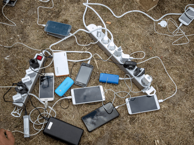 Migrants charge their mobile phones with a generator distributed by the international solidarity organisation Emmaus on May 12, 2017 in Grande-Synthe, northern France. Around 200 Iraqi Kurds live in a nearby forest, a month after the destruction of the migrant camp by a fire. / AFP PHOTO / PHILIPPE HUGUEN …