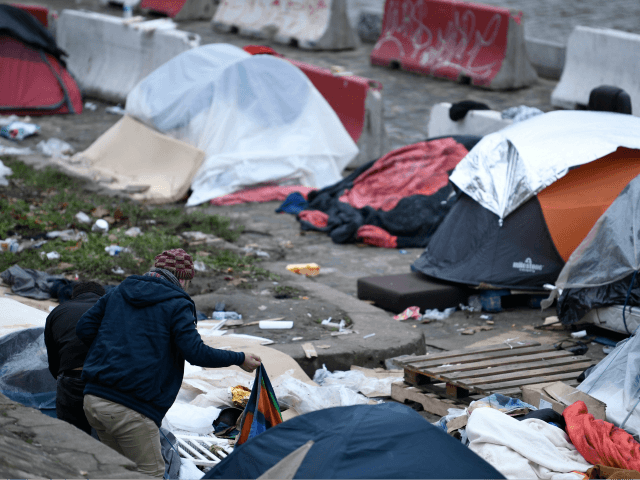 Two men stand next to tents of homeless people, mostly migrants or refugees, by the banks