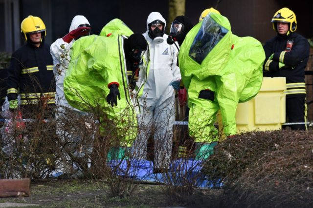 Members of the fire brigade are helped out of their green biohazard suits by colleagues in white protective coveralls after an operation to re-attach the tent over the bench where a man and a woman were found in critical condition sparking a major incident on March 4 at The Maltings …