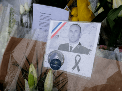 An image Lieutenant-Colonel Arnaud Beltrame is attached to a bouquet of flower laid outside the gates of the gendarmerie of Carcassonne where he worked in southwest France, on March 25, 2018, two days after a man carried out an attack in which he and three other people were killed. Lieutenant-Colonel …