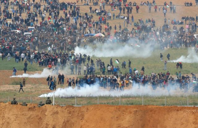 A picture taken on March 30, 2018 from the southern Israeli kibbutz of Nahal Oz across the border from the Gaza strip shows tear gas grenades falling during a Palestinian tent city protest commemorating Land Day, with Israeli soldiers seen below in the foreground. Land Day marks the killing of …