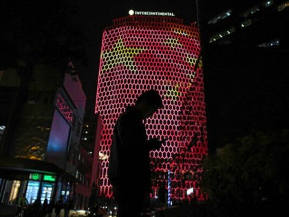 TOPSHOT - A man looks at his phone near a giant image of the Chinese national flag on the