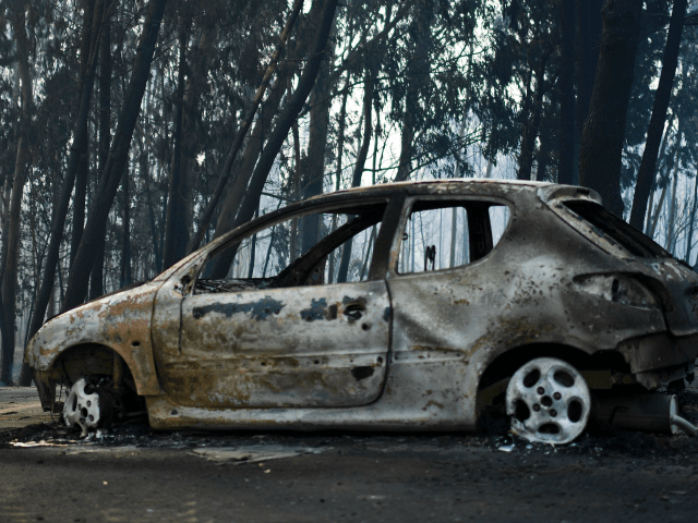 A picture taken on June 18, 2017 shows a burnt car on a road after a wildfire in Pedrogao,