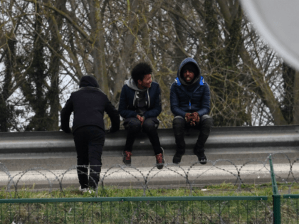 Migrants sit on a crash barrier by the ringroad leading to the harbour on March 30, 2018 i