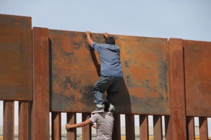 A young Mexican helps a compatriot to climb the metal wall that divides the border between