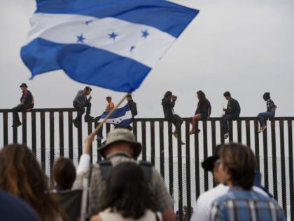 Caravan Migrants climb fence at Mexico/U.S. border.