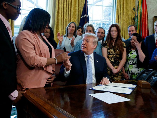 President Donald Trump hands a pen to Yvonne Ambrose who lost her sixteen year-old daughte