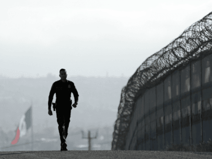 In this Wednesday, June 22, 2016 photo, Border Patrol agent Eduardo Olmos walks near the secondary fence separating Tijuana, Mexico, background, and San Diego in San Diego. The Supreme Court deadlocked Thursday on President Barack Obama's immigration plan that sought to shield millions living in the U.S. illegally from deportation, …