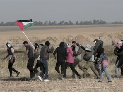 Palestinian masked protesters carrying tires walk toward the border fence during clashes with Israeli troops along Gaza's border with Israel, east of Khan Younis, Gaza Strip, Thursday, April 5, 2018. An Israeli airstrike in northern Gaza early on Thursday killed a Palestinian, while a second man died from wounds sustained …