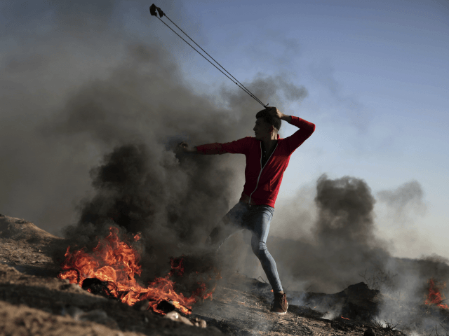 A Palestinian protester hurls stones toward Israeli soldiers during a protest near the Gaza Strip border with Israel, in eastern Gaza City, Saturday, March 31, 2018. (AP Photo/ Khalil Hamra)