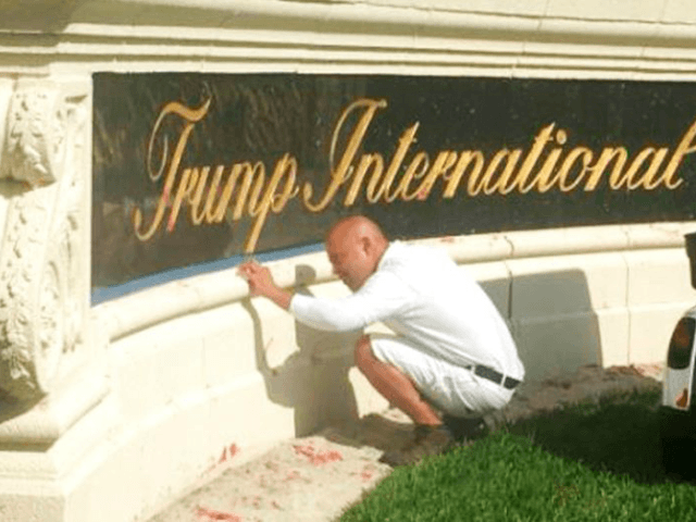 A worker cleans up red paint from the stone sign at the entrance to the Trump International Golf Club in West Palm Beach, Fla., Sunday, April 1, 2018. (WPEC CBS12 via AP)