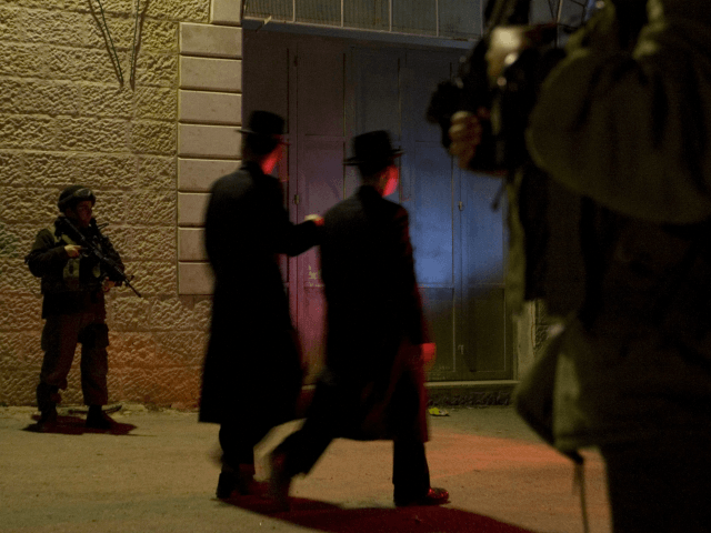 Ultra-Orthodox Jewish men walk past Israeli soldiers as they stand guard next to the tombs