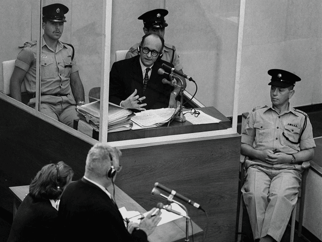 Nazi war criminal Adolph Eichmann stands in a protective glass booth flanked by Israeli po