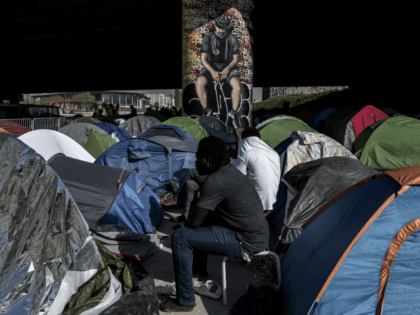 TOPSHOT - Migrants sit by tents at a makeshift camp set under a bridge near Porte de la Villette, northern Paris on April 20, 2018. (Photo by CHRISTOPHE ARCHAMBAULT / AFP) (Photo credit should read CHRISTOPHE ARCHAMBAULT/AFP/Getty Images)