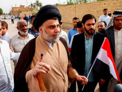 Iraqi Shiite cleric and leader Moqtada al-Sadr (C-L) shows his ink-stained index finger and holds a national flag while surrounded by people outside a polling station in the central holy city of Najaf on May 12, 2018 as the country votes in the first parliamentary election since declaring victory over …