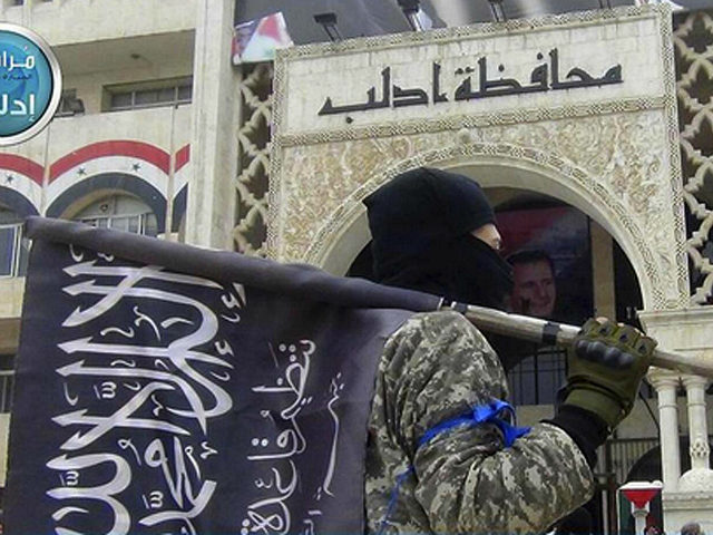 FILE - In this file photo posted on the Twitter page of Syria's al-Qaida-linked Nusra Front on March 28, 2015, which is consistent with AP reporting, a fighter from Syria's al-Qaida-linked Nusra Front holds his group flag as he stands in front of the governor building in Idlib province, north …