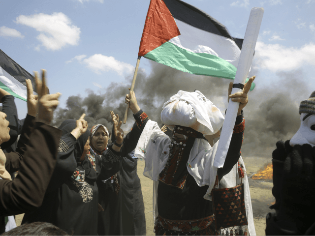 Palestinian women wave national flags and chant slogans near the Israeli border fence, eas