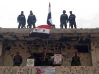 In this photo released by the Syrian official news agency SANA, Syrian military and police forces fly their national flags on a damaged building and hold a picture of Syrian President Bashar Assad, in the Hajar al-Aswad neighborhood, southern Damascus, Syria, Tuesday, May 22, 2018. Syrian state TV said Tuesday …