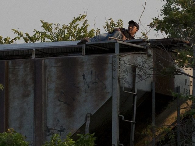 In this Aug. 26, 2014 photo, a migrant lying atop a moving freight train lifts his head to