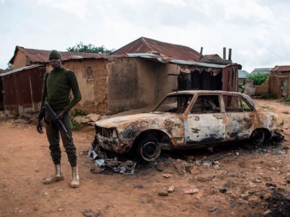 A member of the security forces stands next to a burnt out vehicle in the Nghar Village, n